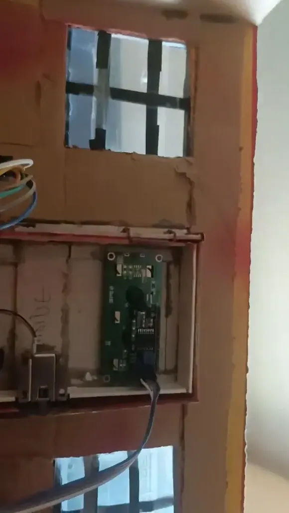 The model house with the circuit board mounted behind its wall and the ribbon cable running to the door